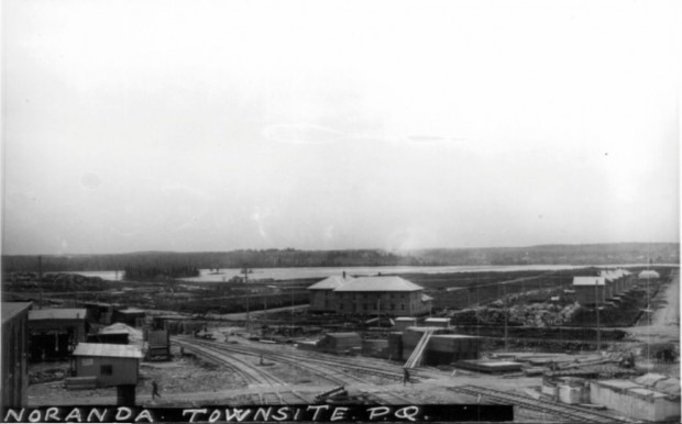photo en noir et blanc du site de la future ville de Noranda. En arrière-plan le lac Osisko, en avant plan, le chemin de fer et à droite les maisons des dirigeants de la mine