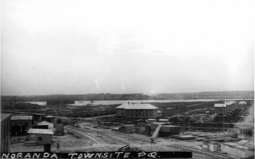 photo en noir et blanc du site de la future ville de Noranda. En arrière-plan le lac Osisko, en avant plan, le chemin de fer et à droite les maisons des dirigeants de la mine