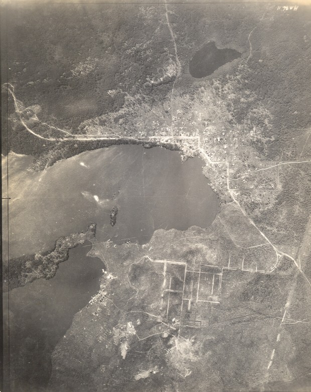 Photographie en noir et blanc, prise à bord d’un avion, de Rouyn et de Noranda à leur tout début. Un lac occupe le centre de la photo. La hauteur à laquelle cette photo a été prise limite beaucoup la vision, mais elle permet de voir que l'agglomération de Rouyn est davantage peuplée que sa voisine Noranda à l’époque .