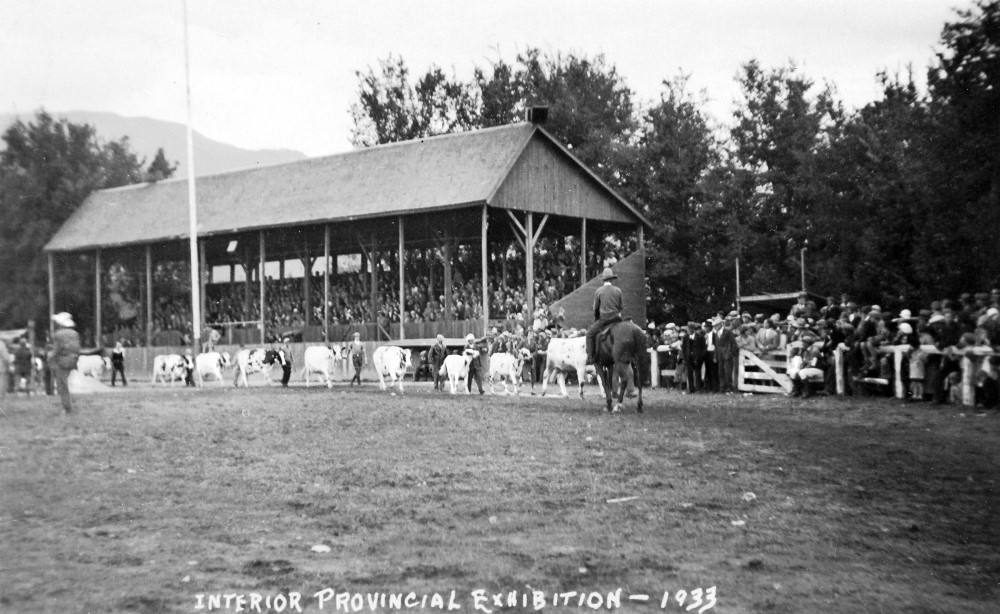 Photo en noir et blanc montrant une tribune pleine et une foule à côté regardant neuf vaches défiler. La mention « Interior Provincial Exhibition 1933 » est inscrite à la main au bas de la photo.