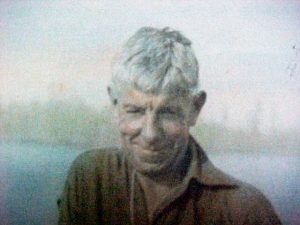 Photo colorée en sépia d’un homme aux cheveux blancs souriant, portant une chemise brune.