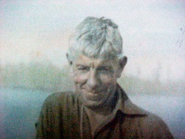 Photo colorée en sépia d’un homme aux cheveux blancs souriant, portant une chemise brune.