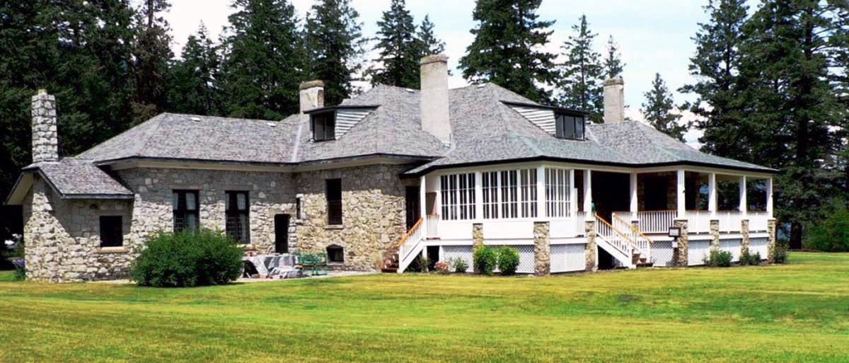 Photo en couleur d’une grande maison en pierre grise avec une véranda blanche.