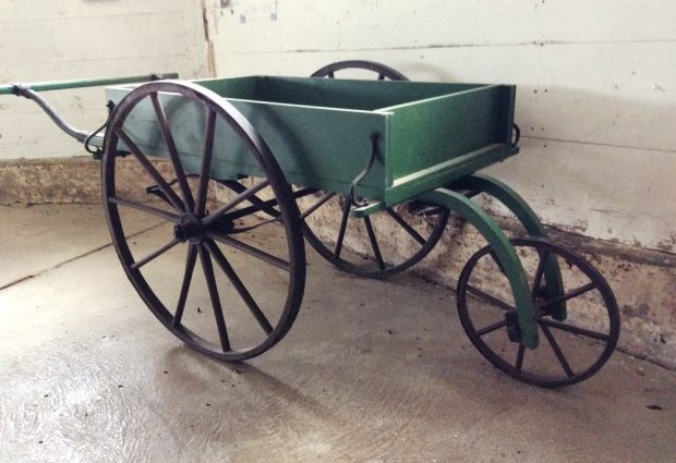 Photo en couleur montrant un grand chariot à main vert avec une petite roue unique à l’avant et deux grandes roues à l’arrière.