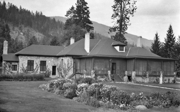 Photo en noir et blanc montrant une grande maison de plain-pied avec une véranda protégée par une moustiquaire.