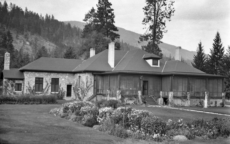 Photo en noir et blanc montrant une grande maison de plain-pied avec une véranda protégée par une moustiquaire.
