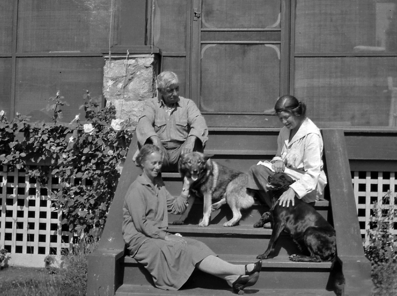 Photo en noir et blanc d’un homme et de deux femmes assis sur un perron.