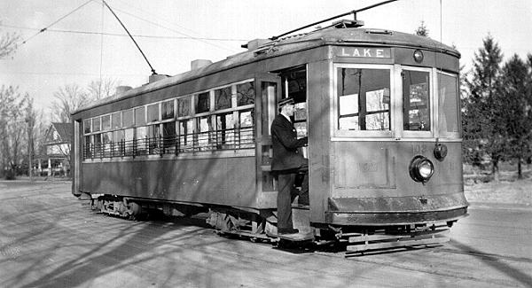  Photographie en noir et blanc d'un tramway électrique et d'une personne à la porte. Le lac est noté sur le devant du tramway électrique.