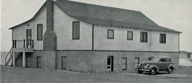 Photographie en noir et blanc d'un bâtiment avec une voiture garée derrière.