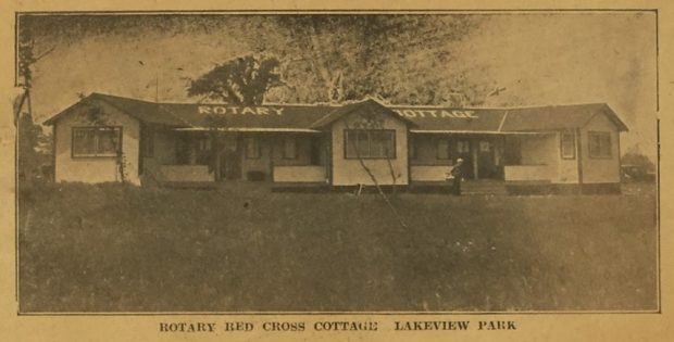 Photographie sépia d'un journal d'un petit immeuble. Rotary Cottage est écrit sur le toit en blanc. La légende indique «Rotary Red Cross Cottage Lakeview Park».
