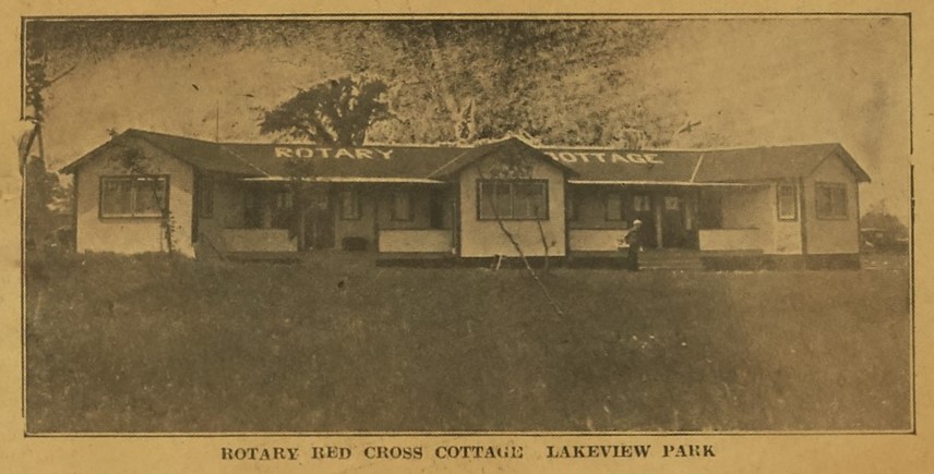 Photographie sépia d'un journal d'un petit immeuble. "Rotary Cottage" est écrit sur le toit en blanc. La légende indique «Rotary Red Cross Cottage Lakeview Park».