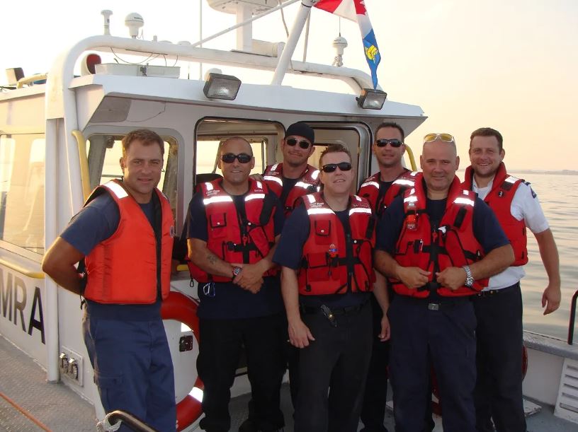  Une photographie en couleur de sept personnes portant des gilets de sauvetage rouges debout sur un bateau.