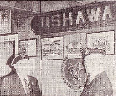 Copie sépia d'une photographie de deux personnes portant des casquettes debout près d'un panneau indiquant Oshawa.