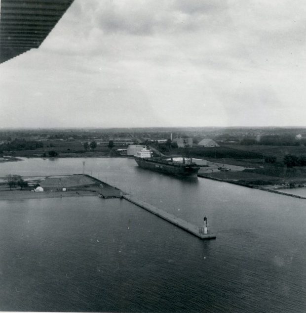  Photographie aérienne en noir et blanc d'un port avec une jetée et un grand navire amarré du côté est.