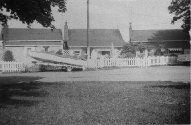 Photographie en noir et blanc de trois chalets et d'un bateau.