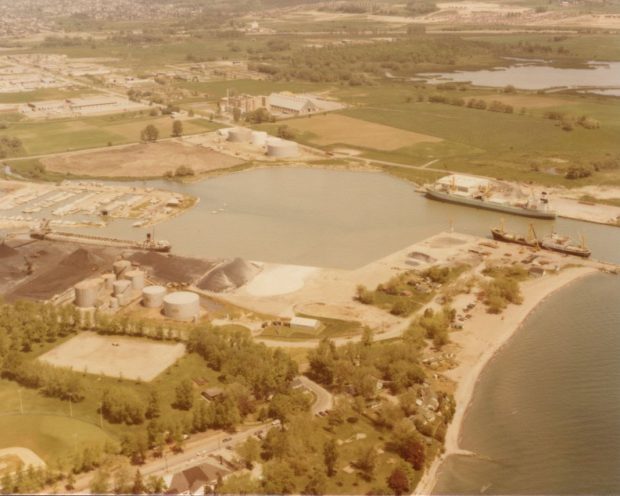 Photographie aérienne en couleur du terrain autour du port d'Oshawa avant l'ouverture de la marina. Il y a trois grands navires amarrés dans le port.