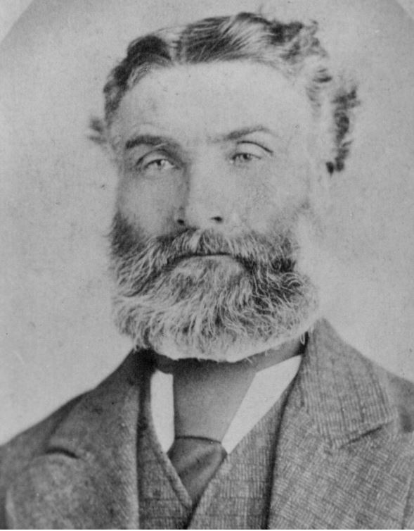 Une photographie en noir et blanc d'une personne avec une barbe portant une veste de costume avec une cravate.