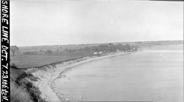 Lame de verre noire et blanche d'un rivage avec un grand plan d'eau. Sur terre il y a des bâtiments et des arbres.