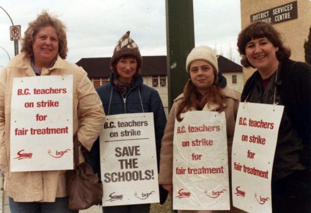 Trois femmes en manteau et chapeau d’hiver se tiennent debout les unes à côté des autres. Elles portent des pancartes sur lesquelles on peut lire « Les enseignants de la C.-B. en grève pour un traitement équitable » et « Les enseignants de la C.-B. en grève, sauvons les écoles! ». Une affiche en arrière-plan indique « Centre de services de district ».