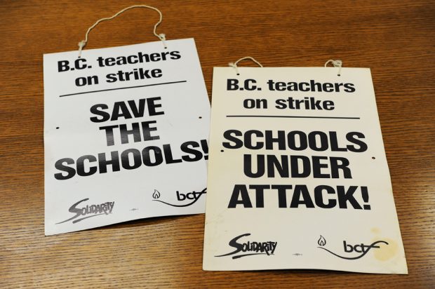 Sur deux pancartes, on peut lire « Les enseignants de la C.-B. en grève, sauvons les écoles » et « Les enseignants de la C.-B. en grève, les écoles attaquées ». 