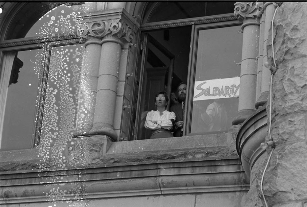 Deux personnes sont présentes à une fenêtre ouverte et une pancarte peinte à la main lit « Solidarity ». 