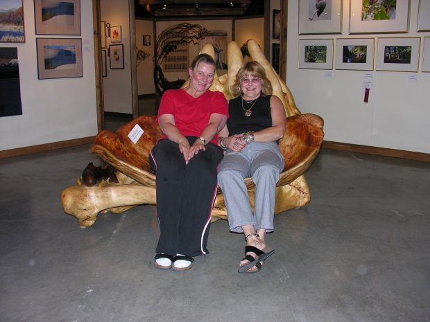 Deux femmes assises sur une sculpture de bois en forme de causeuse.