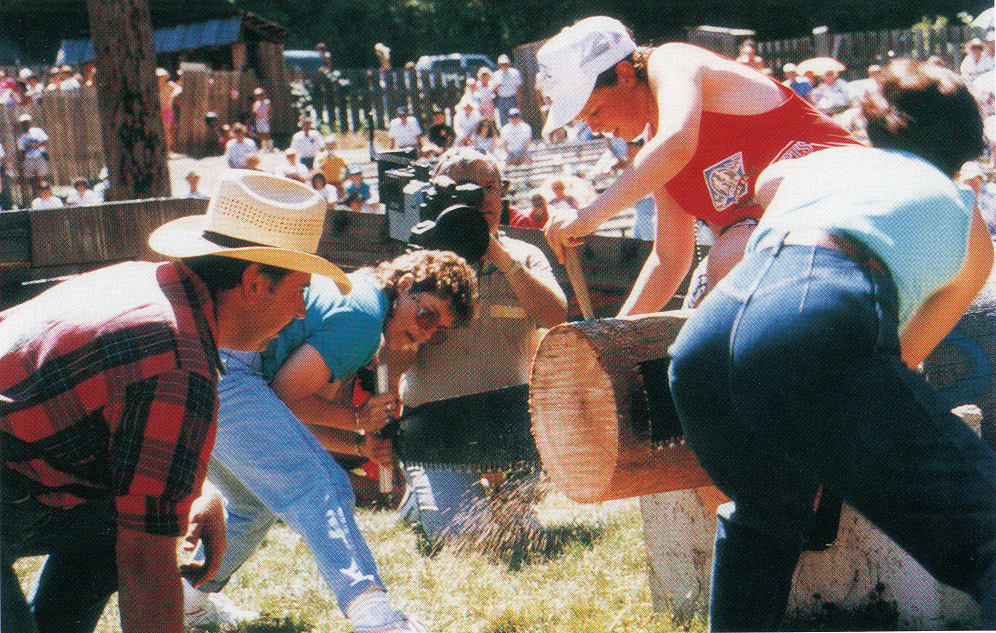 Deux femmes tronçonnant une grume (elles la scient perpendiculairement) sous le regard attentif de la foule.