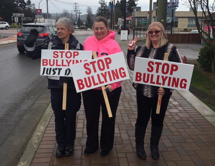 Trois femmes marchant sur un trottoir, tenant des enseignes où on peut lire « Stop Bullying » (Cessez l’intimidation).