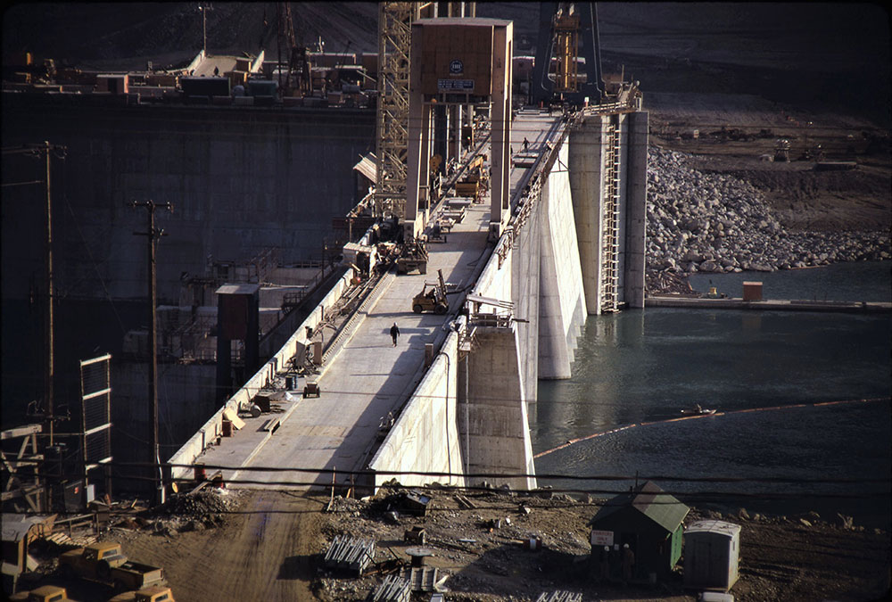 Photographie en gros plan d’un barrage en construction, presque achevé. Des personnes et des véhicules de construction se trouvent sur le barrage.