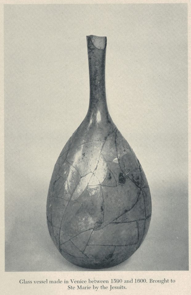Photographie dans les tons sépia d’un contenant en verre intact, avec un col long et fin et un corp large plus étroit au niveau de la base.