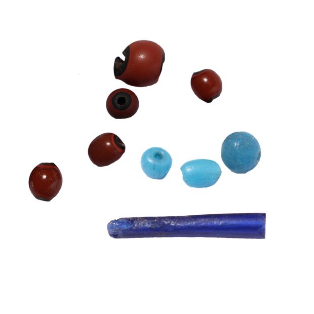 Longue perle bleu foncé, de forme tubulaire, avec trois petites perles rondes bleu clair et cinq perles rondes rougeâtres dont la partie centrale est noire.