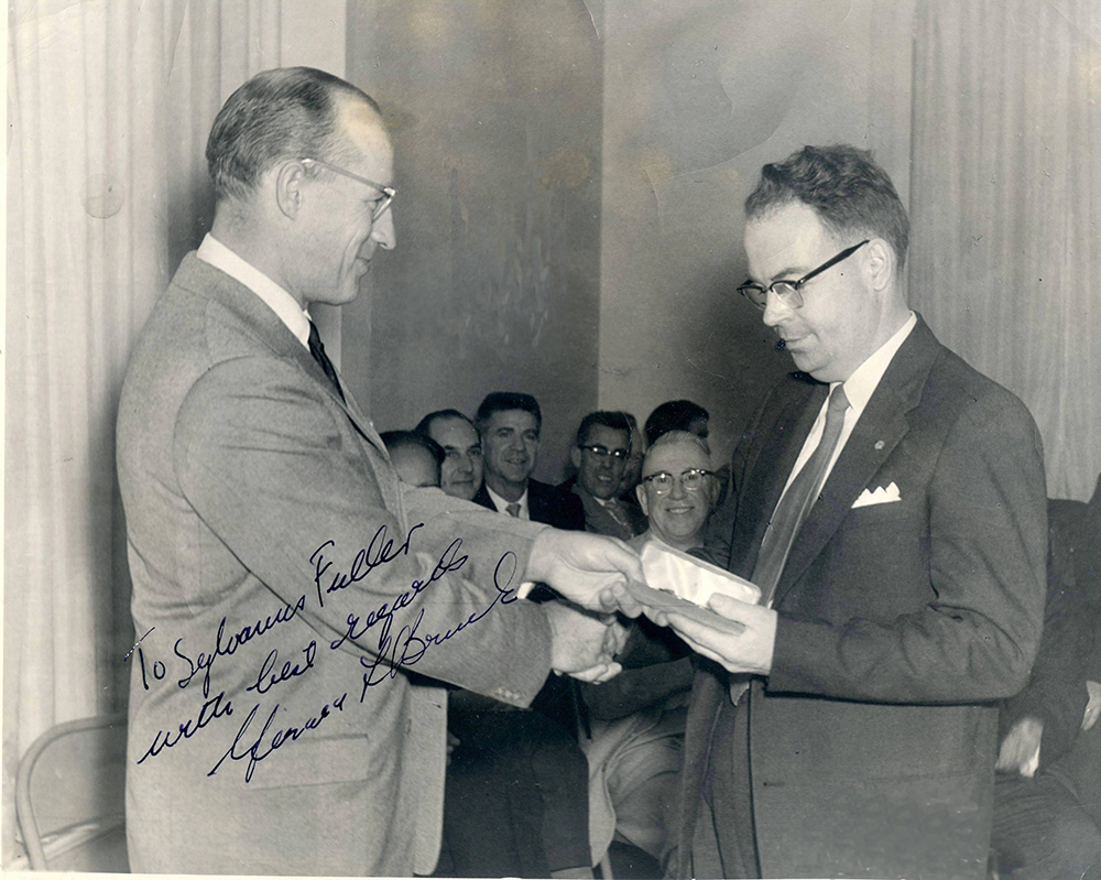 Photo dédicacée par Gerald Bruck montrant la remise d’une montre à l’employé Sylvanus Fuller devant des invités.