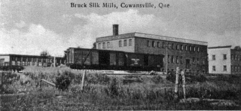 Photo noir et blanc des bâtiments de la Bruck Silk Mills vers 1925 et, à l’avant-plan, un chemin de fer et des wagons.