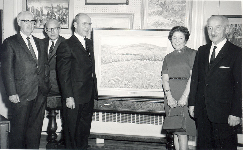 Black and white photo of a lady (Eugenie Lee) surrounded by four men with a framed work in the center.