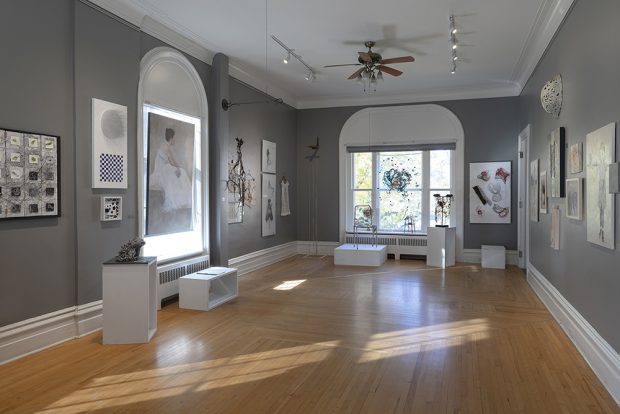 Photo en couleur d'une grande salle avec des oeuvres d'art accrochées sur des murs gris pâle.