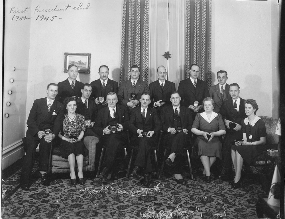 Photo noir et blanc des membres du premier Club du Président posent sur deux rangs avec leur cadeau entre les mains.