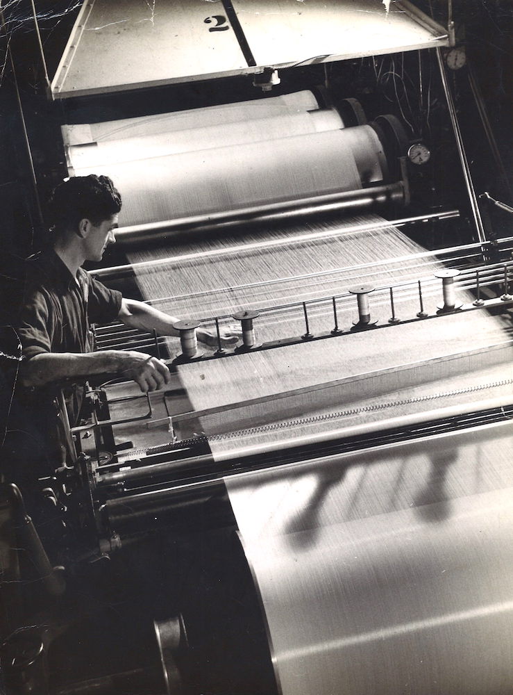 Photo noir et blanc d'un ouvrier penché sur un métier à tisser