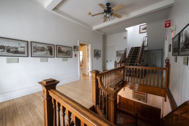 Vue d'une salle avec escalier en bois et photos anciennes en noir et blanc exposées sur les murs