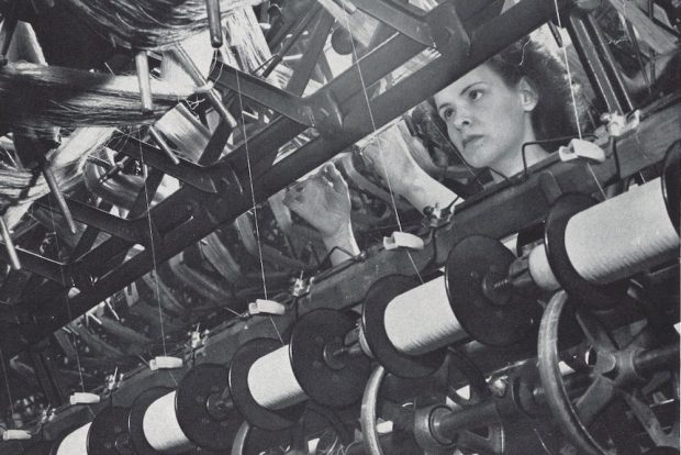 Photo noir et blanc montrant une ouvrière qui regarde des rangées de bobines de fil.