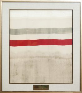 Cadre affichant un morceau de tissu avec une rayure rouge et grise et une plaque l'identifiant comme la première verge de soie tissée au Canada.