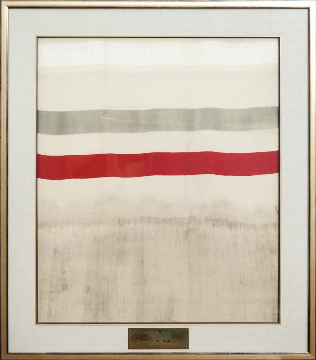 Cadre affichant un morceau de tissu avec une rayure rouge et grise et une plaque l'identifiant comme la première verge de soie tissée au Canada.