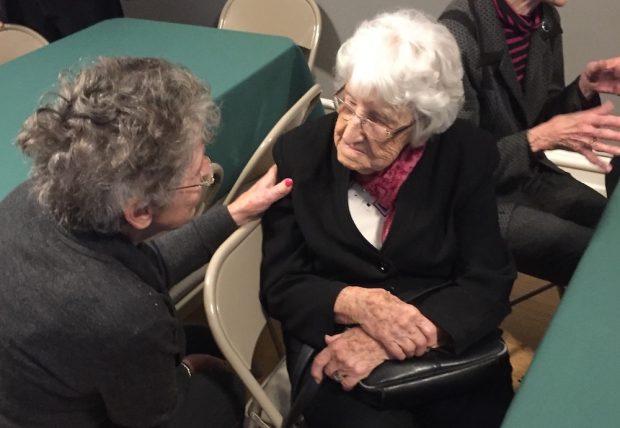 Deux femmes âgées assises à une table discutent entre elles.