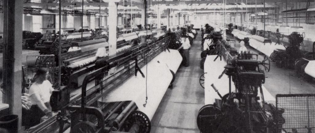 Salle dans une usine avec plusieurs rangées de machines à tisser.