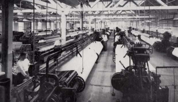 Salle dans une usine avec plusieurs rangées de machines à tisser.