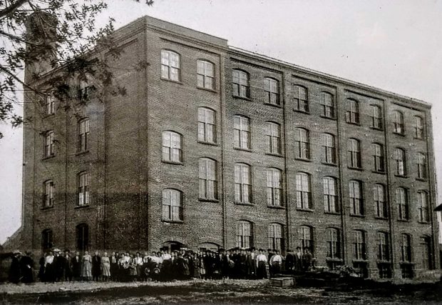 Photographie en noir et blanc d'une usine avec un groupe de personnes devant.