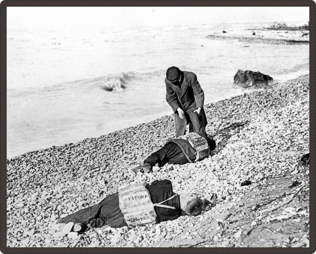 Photo en noir en noir et blanc d’un homme examinant deux corps inanimés sur la plage.