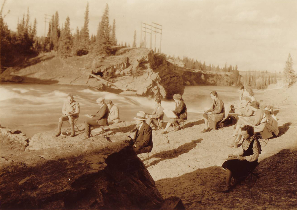 Photo sépia d’un groupe d’artistes faisant des croquis sur la berge d’une rivière dans un paysage boisé et rocheux.