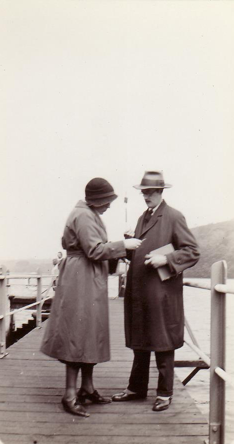 Photo noir et blanc d’un couple habillé élégamment, debout sur le quai, consultant quelque chose que la femme tient à la main.