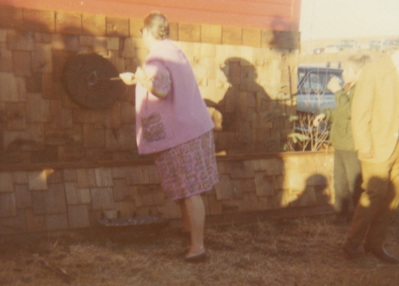 Photo couleur d’une femme de dos, avec un fer à marquer à la main, en train de marquer un objet circulaire sur un mur extérieur.