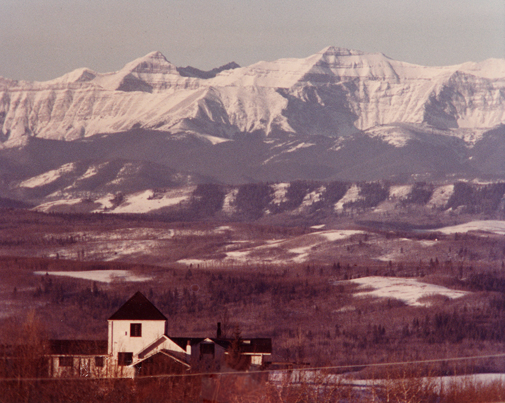 Photo aérienne en couleur d’une maison noire et blanche avec des collines et des montagnes au loin.